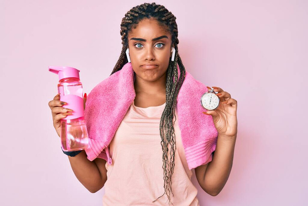 Saçları örülmüş, elinde su şişesi olan genç Afro-Amerikan spor kadın şüpheci ve gergin, sorun yüzünden üzgün. negatif kişi.  - Fotoğraf, Görsel