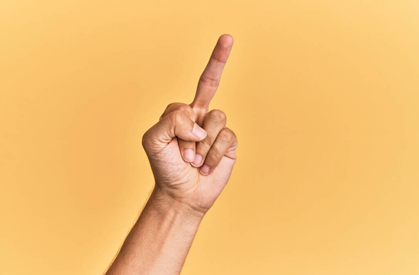 Рука і рука кавказького чоловіка над жовтим ізольованим тлом, що показує провокаційний і грубий жест роблять хуй ви символ з середнім пальцем
  - Фото, зображення