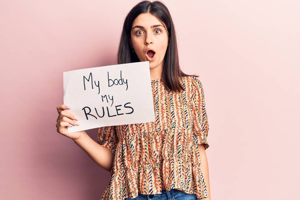 Young beautiful girl holding my body my rules banner scared and amazed with open mouth for surprise, disbelief face  - Photo, Image