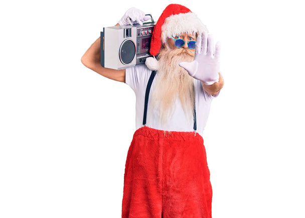 Oude senior man met grijs haar en lange baard in kerstman kostuum en boombox met open hand doen stopbord met serieuze en zelfverzekerde uitdrukking, verdediging gebaar  - Foto, afbeelding