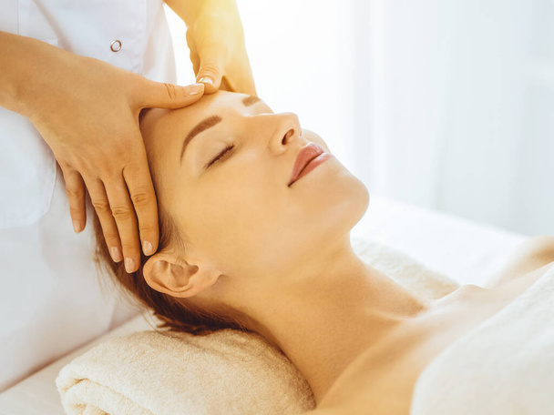 Güneşli spa merkezinde yüz masajından hoşlanan güzel bir kadın. Tıpta rahatlatıcı tedavi kavramı - Fotoğraf, Görsel