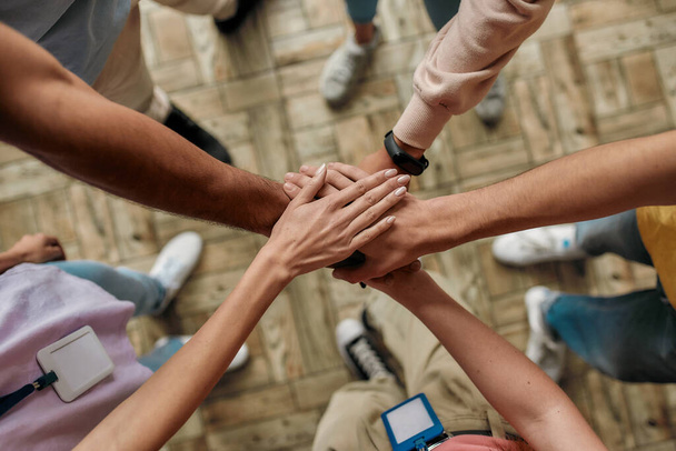 Top view of diverse young volunteers putting their hands on top of each other like a real team while standing in charitable organization office - Φωτογραφία, εικόνα