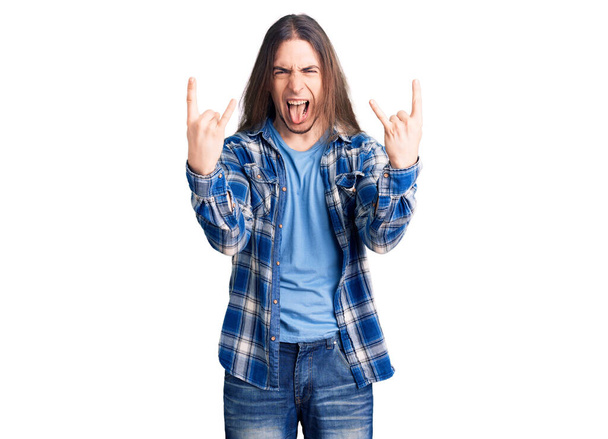 Young adult man with long hair wearing casual shirt shouting with crazy expression doing rock symbol with hands up. music star. heavy concept.  - Foto, Imagen