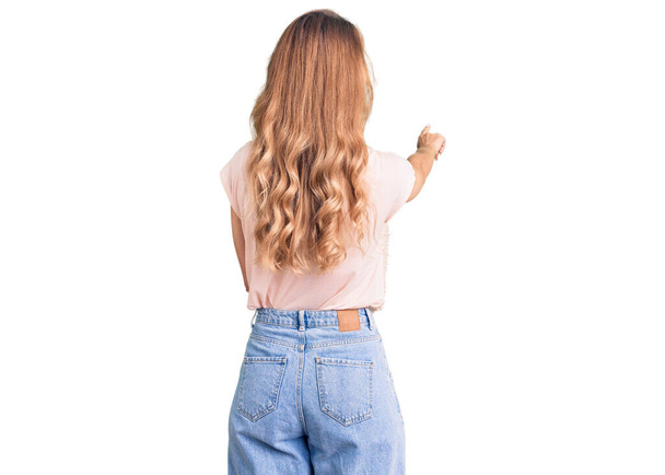 Νεαρή όμορφη καυκάσια γυναίκα με ξανθά μαλλιά φορώντας καθημερινά ρούχα που ποζάρουν προς τα πίσω δείχνοντας μπροστά με το χέρι δάχτυλο  - Φωτογραφία, εικόνα