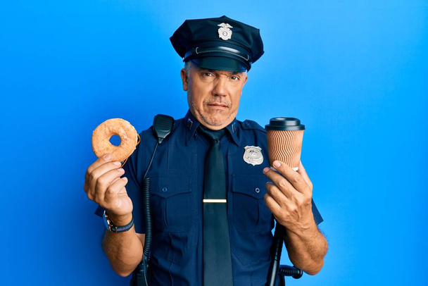 Handsome middle age mature police man eating donut and drinking coffee clueless and confused expression. doubt concept.  - Фото, зображення