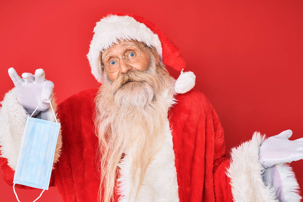Alter älterer Herr im Weihnachtsmann-Kostüm mit Schutzmaske feiert Leistung mit glücklichem Lächeln und Siegerausdruck mit erhobener Hand  - Foto, Bild