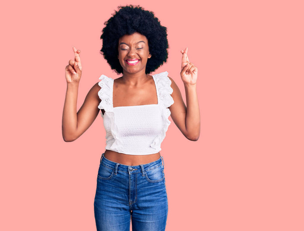 Giovane donna afroamericana che indossa abiti casual gesticolando dito incrociato sorridendo con speranza e gli occhi chiusi. fortuna e concetto superstizioso.  - Foto, immagini