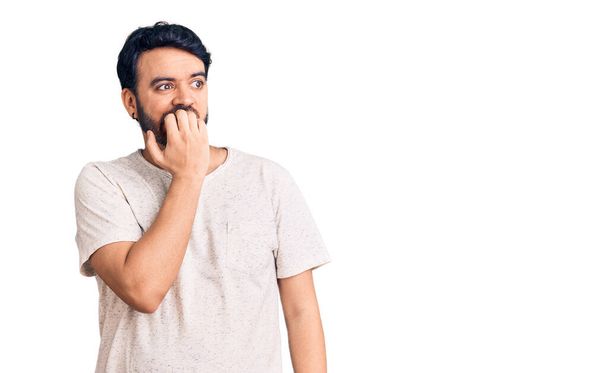 Jonge Spaanse man draagt casual kleding die er gestrest en nerveus uitziet met handen op de mond bijtende nagels. angstprobleem.  - Foto, afbeelding