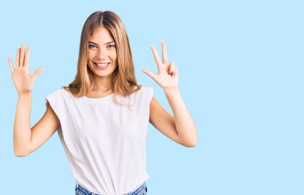 Beautiful caucasian woman with blonde hair wearing casual white tshirt showing and pointing up with fingers number eight while smiling confident and happy.  - Photo, Image