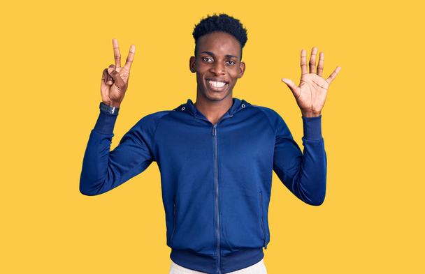 Młody Afroamerykanin w odzieży sportowej, pokazujący i wskazujący palcami numer siedem, uśmiechnięty, pewny siebie i szczęśliwy..  - Zdjęcie, obraz