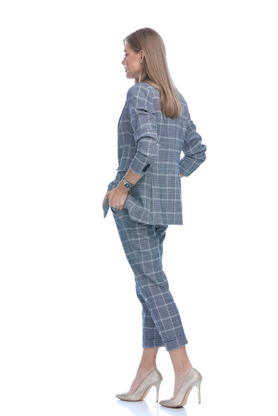 side view of young businesswoman in blue checkered suit holding hand sin pockets and standing isolated on white background, full body - Zdjęcie, obraz