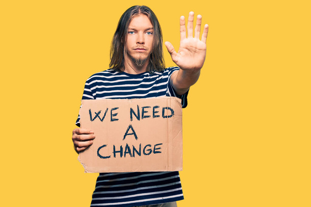 Handsome caucasian man with long hair holding we need a change banner with open hand doing stop sign with serious and confident expression, defense gesture  - Photo, Image