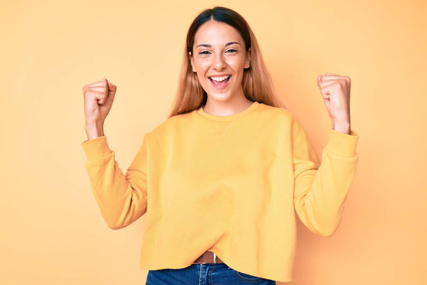 Young brunette woman over yellow background screaming proud, celebrating victory and success very excited with raised arms  - Photo, Image