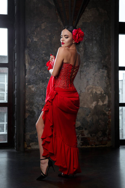 Portrait of a sultry brunette woman in a long red dress with a deep neckline and a red flower in her hair in the castle interior. - Fotoğraf, Görsel
