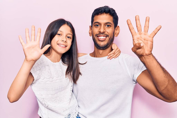 Jonge vader en dochter dragen casual kleding tonen en wijzen met vingers nummer negen, terwijl ze vol vertrouwen en gelukkig glimlachen.  - Foto, afbeelding