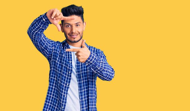 Handsome latin american young man wearing casual shirt smiling making frame with hands and fingers with happy face. creativity and photography concept.  - Foto, Imagen