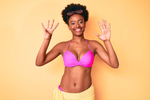 Jovem afro-americana vestindo biquíni mostrando e apontando para cima com os dedos número nove enquanto sorri confiante e feliz.  - Foto, Imagem