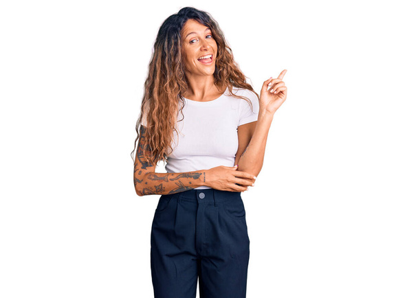 Young hispanic woman with tattoo wearing casual white tshirt with a big smile on face, pointing with hand and finger to the side looking at the camera.  - Φωτογραφία, εικόνα