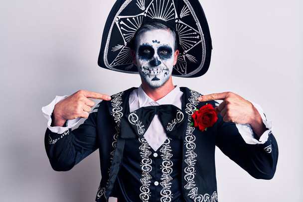 Giovane uomo che indossa il giorno messicano del costume morto su bianco guardando fiducioso con il sorriso sul viso, puntandosi con le dita orgoglioso e felice.  - Foto, immagini