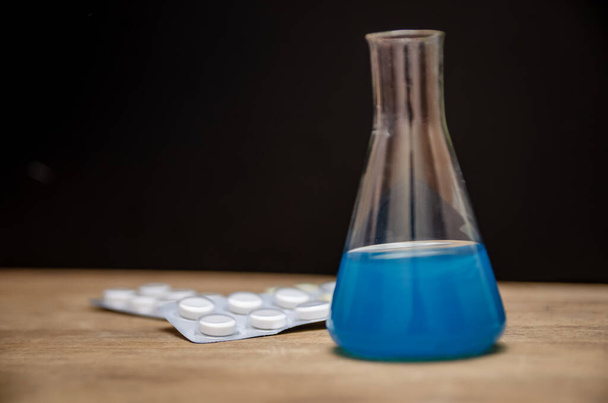 Flask met blauwe oplossing en pillen n zwarte achtergrond close-up. Geneeskundig concept, lab - Foto, afbeelding