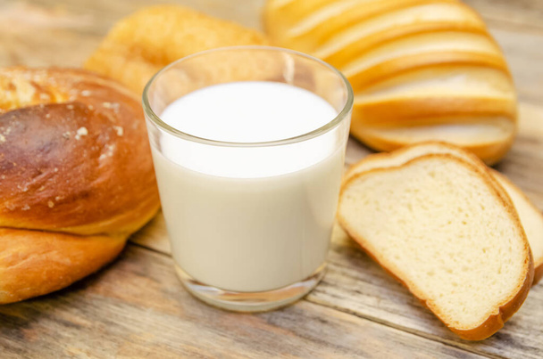 Glass of milk, rolls, sliced loaf on a wooden background - 写真・画像