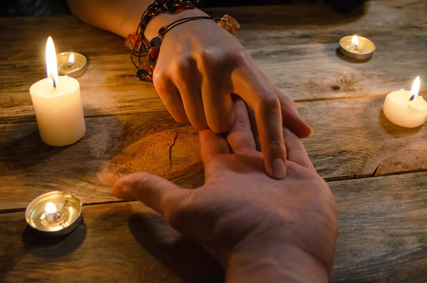 kobieta wróżka czyta linie męskiej ręki i przepowiada jego przyszłość, ręce na drewnianym tle wśród świec. koncepcja magii, wróżby - Zdjęcie, obraz