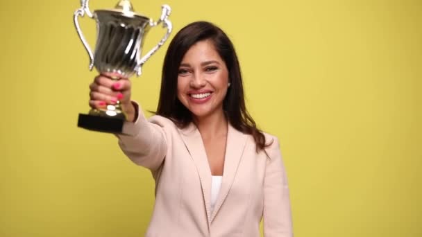 atrakcyjna bizneswoman podnosząc swoje trofeum, wskazując na aparat, tańcząc pełen radości i świętując zwycięstwo na żółtym tle - Materiał filmowy, wideo