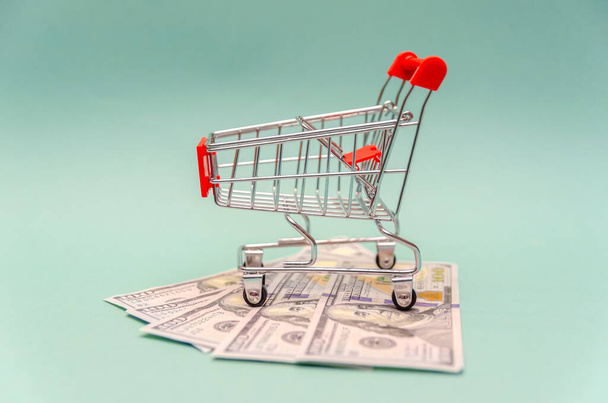 roter Einkaufswagen steht auf Dollarscheinen auf blauem Hintergrund. Konzept Online-Shopping, Online-Shopping - Foto, Bild