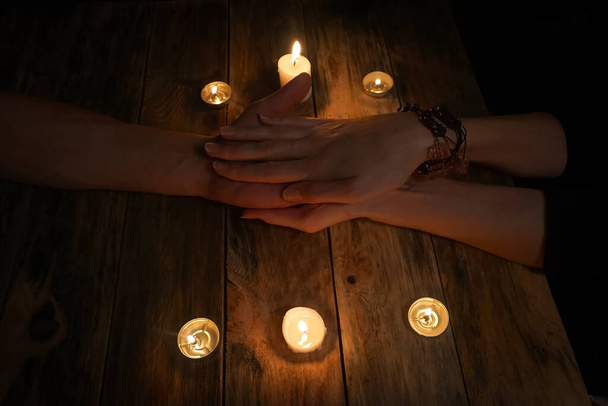 waarzegster houdt de hand van een man in haar eigen op een houten tafel tussen de kaarsen. concept van magie, waarzeggerij - Foto, afbeelding