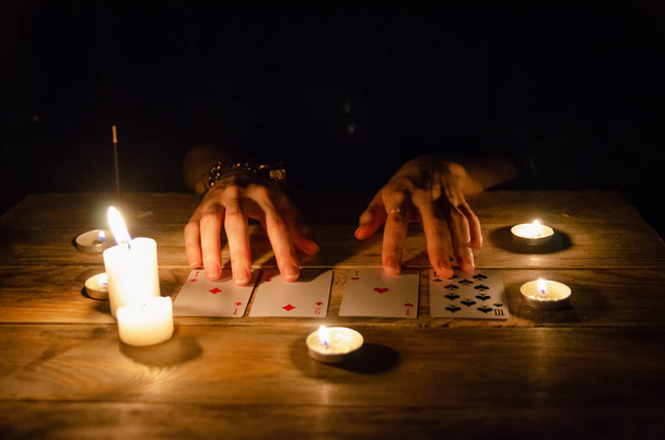 Manos de adivino y cartas sobre la mesa, alrededor de velas encendidas en la oscuridad sobre una mesa de madera. concepto de adivinación, magia - Foto, imagen
