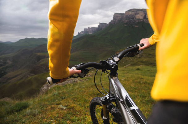 Close-up of female hands holding handlebars of mountain bike outdoors on green grass background - 写真・画像
