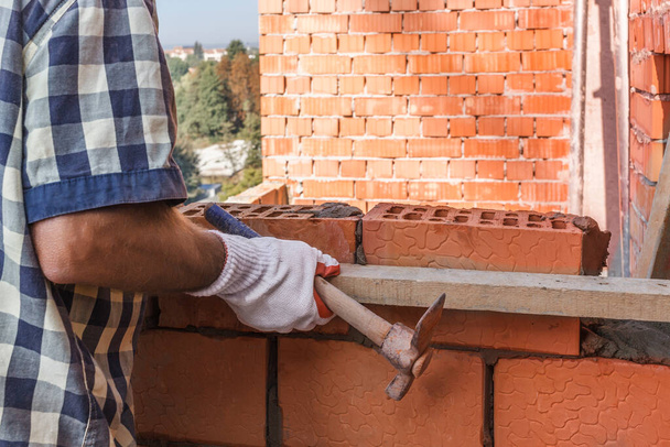 A bricklayer in protective gloves with a trowel places a brick on the mortar on the wall - Photo, Image