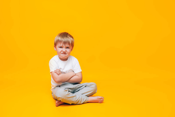Weinender kleiner Junge reibt sich die Augen mit den Händen, ein Junge in weißem T-Shirt auf gelbem Hintergrund. - Foto, Bild
