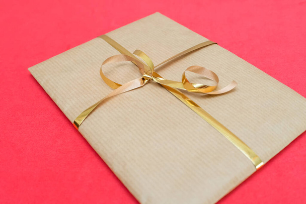 Craft gift packaging with a gold ribbon on a red background - Photo, Image