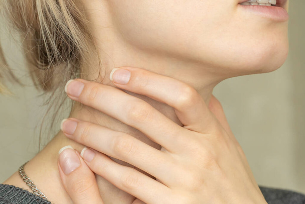 Girl holds her hands to her throat, sore throat. Close-up of the girl's hands touching the sore throat. - Foto, Bild