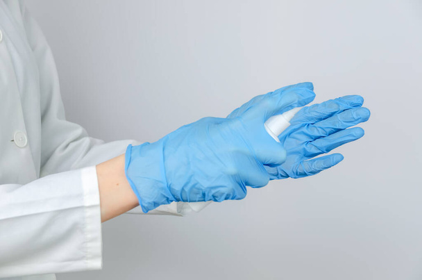 doctor in a white coat and blue gloves disinfects his hands with an antiseptic spray close up - Фото, зображення