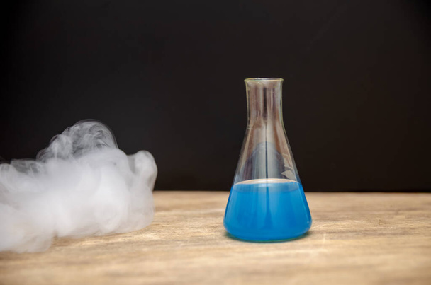 baňka s modrou tekutinou v kouři na černém pozadí. chemická analýza - Fotografie, Obrázek