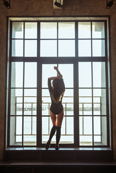 Silhouette of a slim athletic girl on a background of a large window. - Foto, Imagem
