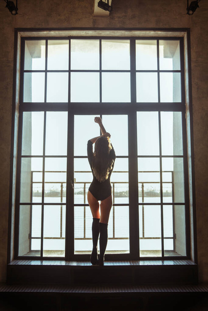Silhouette of a slim athletic girl on a background of a large window. - Foto, imagen
