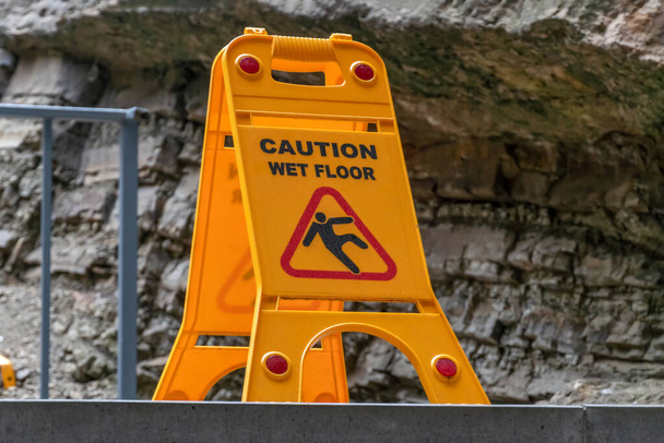 предупреждение желтый знак "влажный пол" на фоне части скалы, горы крупным планом - Фото, изображение