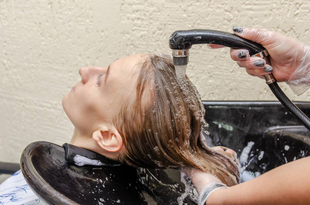 Proces mycia włosów z fioletowego barwnika w zakładzie fryzjerskim. Mycie farby wodą pod kranem u fryzjera. blondynka w salonie piękności. - Zdjęcie, obraz