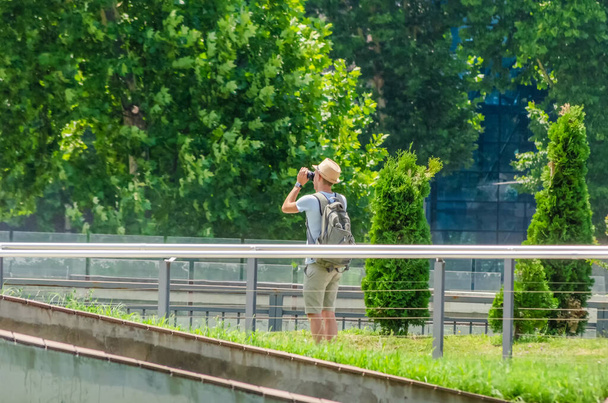Photography or the concept of the traveler. Man traveler in shorts, t-shirt, hat and backpack taking pictures in the city on a Sunny day - Fotó, kép