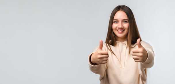 Happy Pretty young woman with long chestnut hair, Smiling and showing thumbs up, dressed in casual clothes. I like that. Good job.Human emotions concept. Copy space for your text - Photo, Image