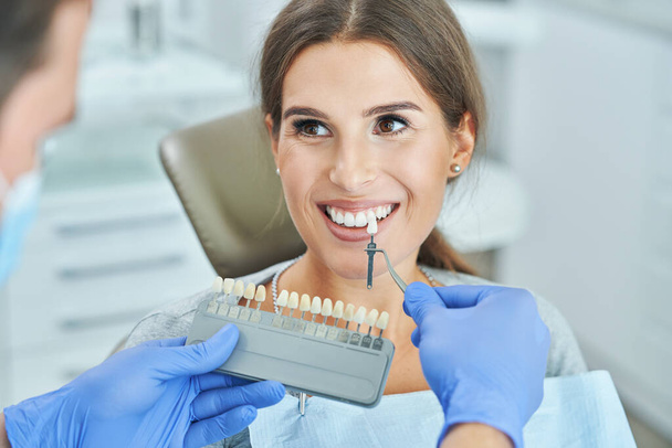 Male dentist and woman choosing tooth shade in dentist office - Fotó, kép