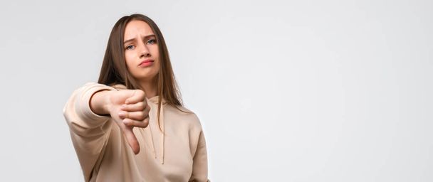 Young woman with long chestnut hair, dressed in casual clothes, looking unhappy and angry showing dislike with thumb down, rejection concept. Copy space for your text - Foto, immagini