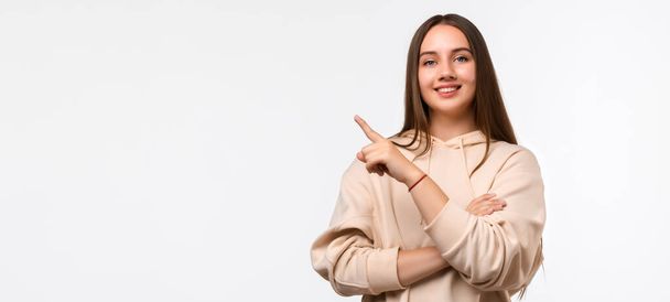 Happy Pretty young woman with long chestnut hair, pointing finger to the side, shows copy space for your information. Studio shot, white background - Photo, Image