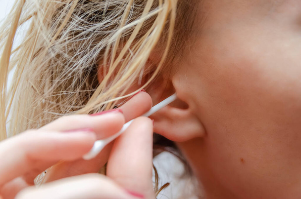 Blonde γυναίκα καθαρίζει το αυτί της με ένα λευκό βαμβάκι μάκτρο από κοντά - Φωτογραφία, εικόνα
