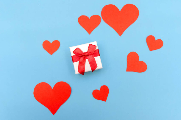 Caja de regalo entre corazones de papel rojo sobre un fondo azul. Vista superior, espacio de copia. Día de San Valentín, un símbolo de amor. Fondo festivo - Foto, Imagen