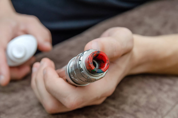 man disinfects an electronic cigarette with an aerosol antiseptic close up - Zdjęcie, obraz