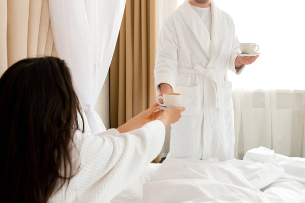 Ο άντρας φέρνει καφέ στην κοπέλα του ξαπλωμένη στο κρεβάτι. - Φωτογραφία, εικόνα